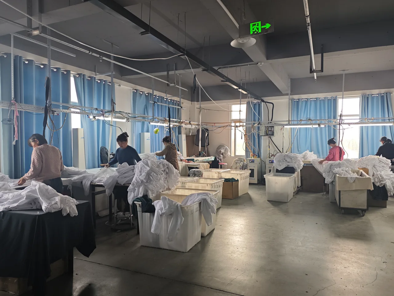Workers handling garments at finishing stations beside windows in the workshop